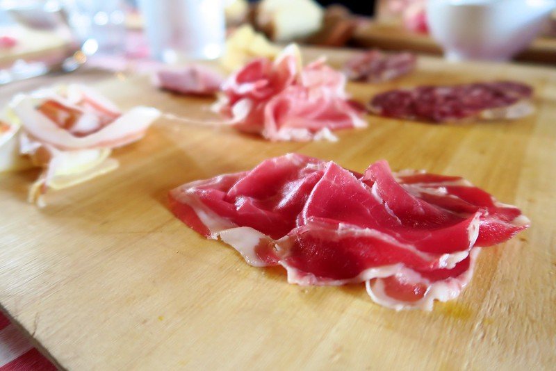 Close-up of thinly sliced Culatello di Zibello, a prized cured meat from Emilia-Romagna, Italy, served on a wooden board during a traditional tasting experience, highlighting the rich flavors and artisanal charcuterie culture of the region