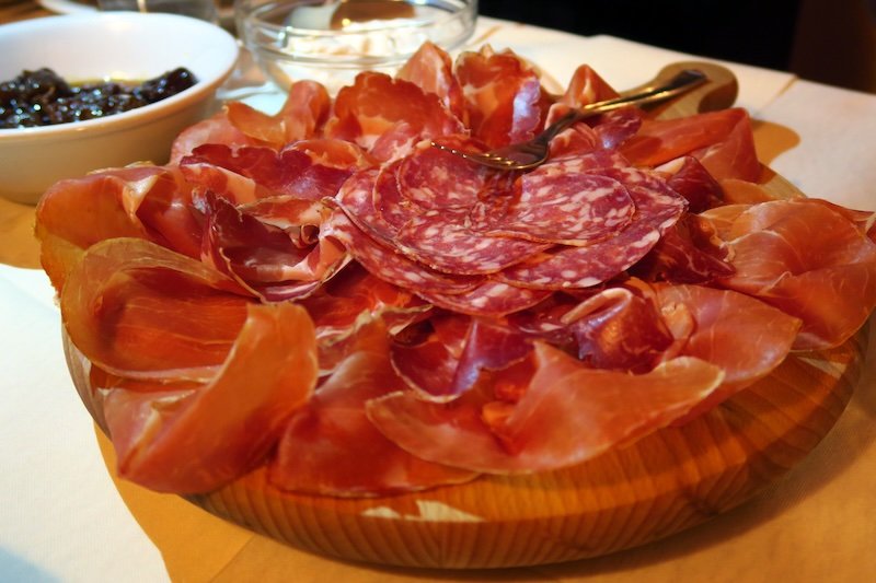 Platter of assorted cured meats in Emilia-Romagna, Italy, including prosciutto, salami, and coppa, beautifully arranged on a wooden board and served with condiments, showcasing the region’s world-renowned charcuterie and traditional food culture