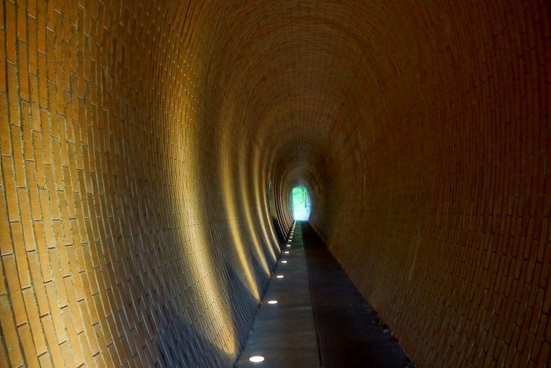 Curved underground brick tunnel with warm lighting leading to a bright exit framed by greenery in Prague, Czech Republic