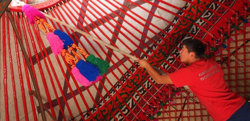 Decorating the interior of a Kyrgyz yurt in Kyzyl-Tuu using a pole to add the final touches of detail 