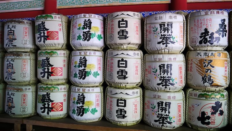 Stacked decorative sake barrels wrapped in straw with colourful Japanese calligraphy and designs, displayed as ceremonial offerings at a shrine in Nikko, Japan