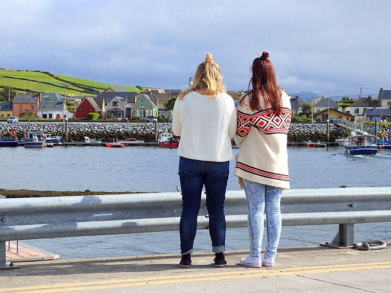 Dingle Harbour in Ireland with views of boats docked and cute colorful homes dotting the waterfront area with the girls road trip ganging taking it all in
