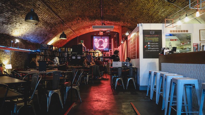 Interior of Draughts board game café in London with cozy arched brick ceilings, neon wall art, and shelves of games, where visitors gather to play, eat, and relax in a lively social atmosphere blending modern design with the city’s historic charm