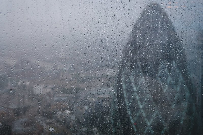 Rain-speckled window view of London’s iconic Gherkin skyscraper as seen from Duck & Waffle restaurant, capturing the city’s misty skyline on a rainy day and showcasing the unique high-rise dining perspective of this famous rooftop venue
