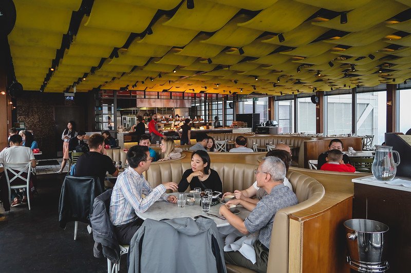 Interior of Duck & Waffle restaurant in London, featuring diners enjoying meals in the modern rooftop setting with panoramic windows and bold yellow ceiling design, offering one of the city’s most unique dining experiences high above the skyline
