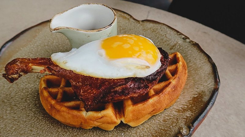Close-up of the iconic Duck & Waffle dish in London, featuring crispy duck leg served on a golden waffle topped with a fried egg and accompanied by a small pitcher of syrup, highlighting one of the city’s most famous high-rise dining experiences