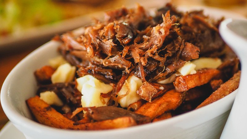 A decadent bowl of gourmet poutine topped with shredded duck confit, cheese curds, and rich brown gravy at À L’Abordage Microbrasserie in Sutton, Quebec, showcasing the region’s creative twist on this poutine classic