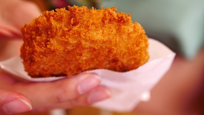 Eating cheese korokke in Kamakura's walking street with its flaky exterior is a high calorie street food snack in Japan Eating cheese korokke in Kamakura's walking street with its flaky exterior is a high calorie street food snack in Japan
