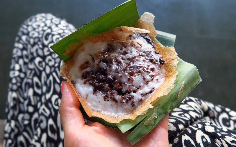 Eating serabi (coconut pancakes) in Solo, Indonesia as a delicious and sweet street food snack served traditionally in a wrapper 