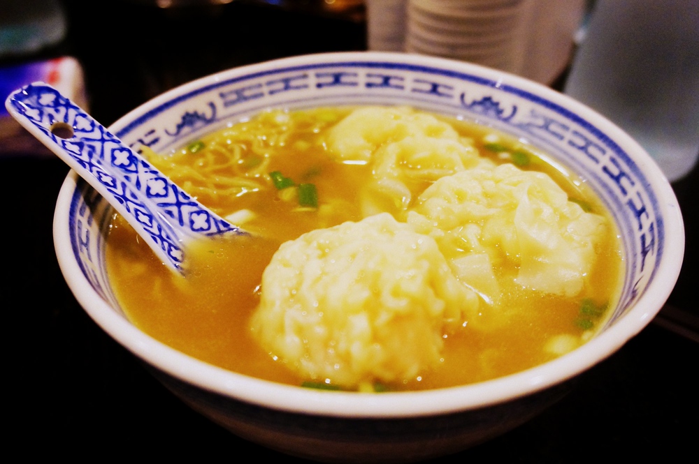 Eating wonton noodle soup with pork wontons in Hong Kong served in a bowl with a large spoon 