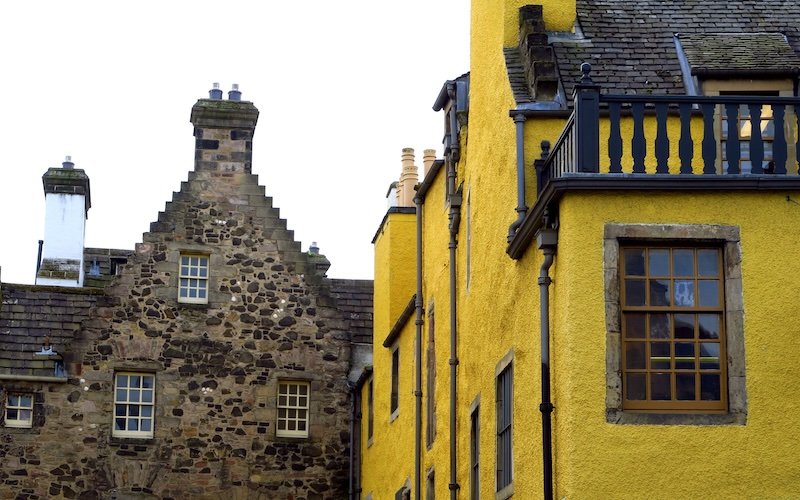 Historic architecture in Edinburgh’s Old Town featuring a bright yellow plastered building alongside a stone gabled house with chimneys