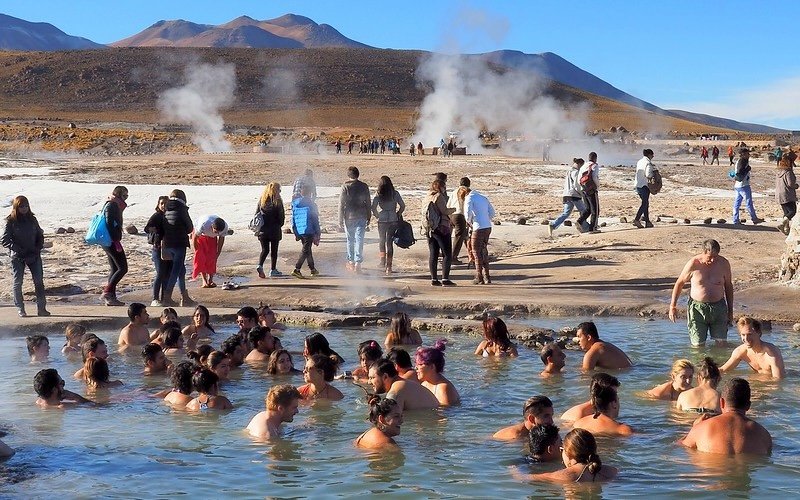 Travelers soaking in the thermal hot springs at El Tatio Geysers in the Atacama Desert, Chile, with steam rising in the background