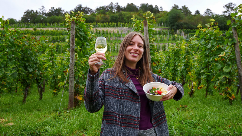 Enjoying a vineyard picnic at Herzoglicher Weinberg in Freyburg, Germany with That Backpacker Audrey Bergner holding a glass of wine and food in the other hand