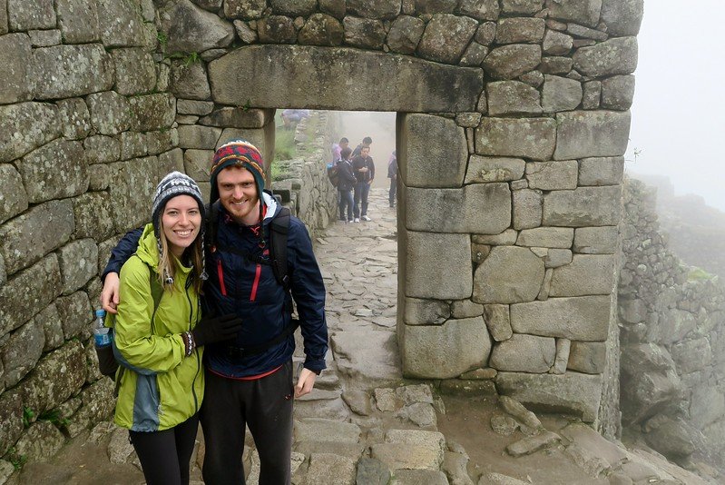 Entering Machu Picchu, Peru is a smiling but wet Nomadic Samuel and Audrey Bergner That Backpacker wearing Peruvian hats after their hike