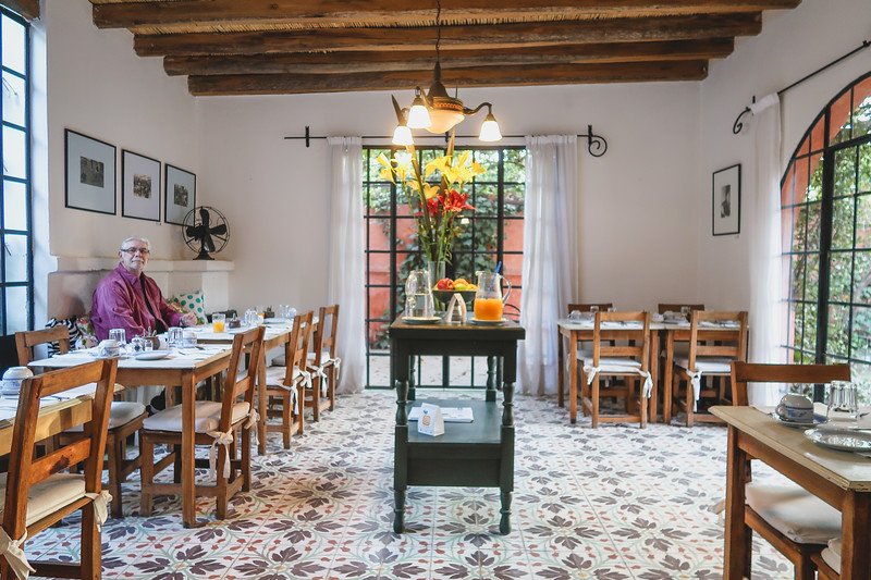 Breakfast is served at Finca Adalgisa in Mendoza, Argentina. The bright dining room features patterned tile floors, wooden beams, and large windows opening to the garden. Daniel Bergner enjoys breakfast at one of the tables, adding a warm, personal touch
