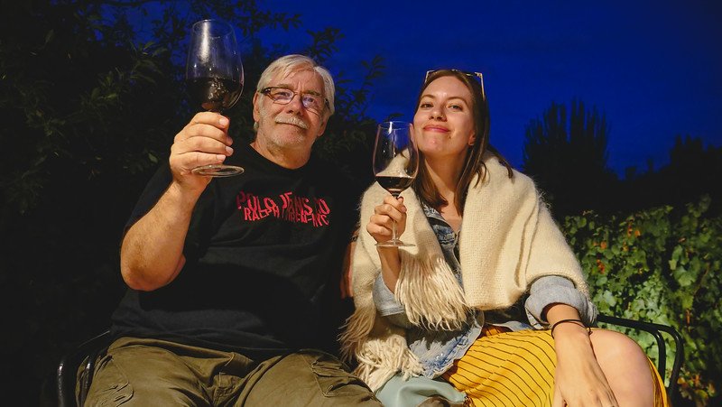 Audrey Bergner of That Backpacker and her father, Daniel Bergner, enjoying a complimentary wine tasting at Finca Adalgisa in Mendoza, Argentina. They raise their glasses of Malbec under the night sky, sharing a warm father-daughter travel moment