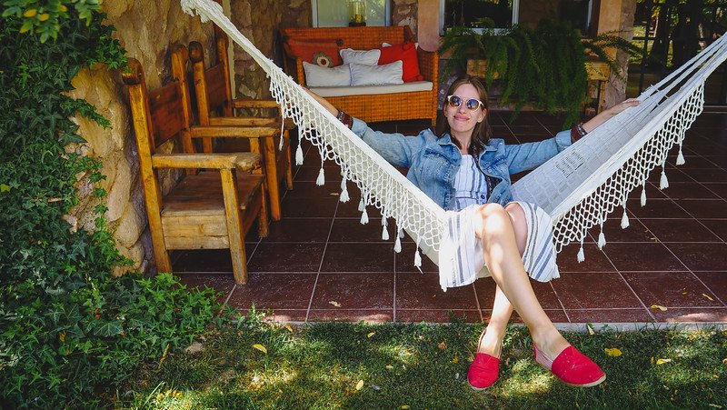 Audrey Bergner of That Backpacker lounging on a white hammock at Finca Adalgisa, a boutique wine hotel in Mendoza, Argentina. She’s wearing a denim jacket, striped dress, and red espadrilles, enjoying a peaceful afternoon on the shaded terrace