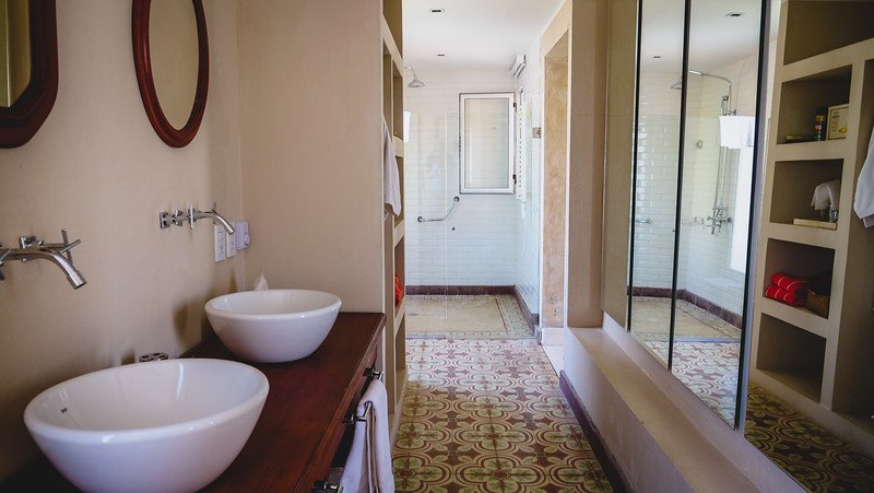 The spacious suite bathroom at Finca Adalgisa, a boutique wine hotel in Mendoza, Argentina. It features dual vessel sinks, a large walk-in shower, patterned tile floors, and built-in shelving, combining rustic charm with modern comfort for a high-end stay