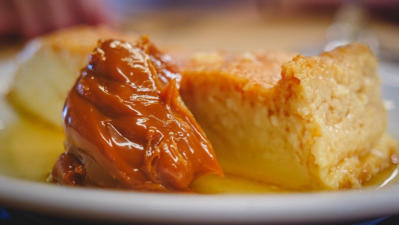 Close-up of a traditional Argentine dessert featuring creamy flan served with a generous spoonful of rich dulce de leche, enjoyed at Estancia San Lorenzo on Península Valdés, Patagonia. The smooth caramel and custard textures highlight local culinary traditions