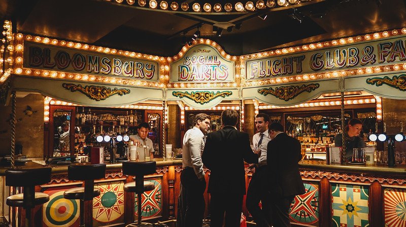 Group of friends enjoying a night out at Flight Club in London, a lively social darts bar with retro carnival décor, illuminated signage, and a buzzing atmosphere that combines classic pub vibes with interactive games and cocktails