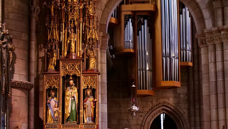 Close-up of the ornate gilded altar statues and towering silver organ pipes inside the Gothic Freiburg Cathedral (Freiburger Münster) in Freiburg im Breisgau, Germany, where visitors can enjoy the majestic sound of the cathedral organ