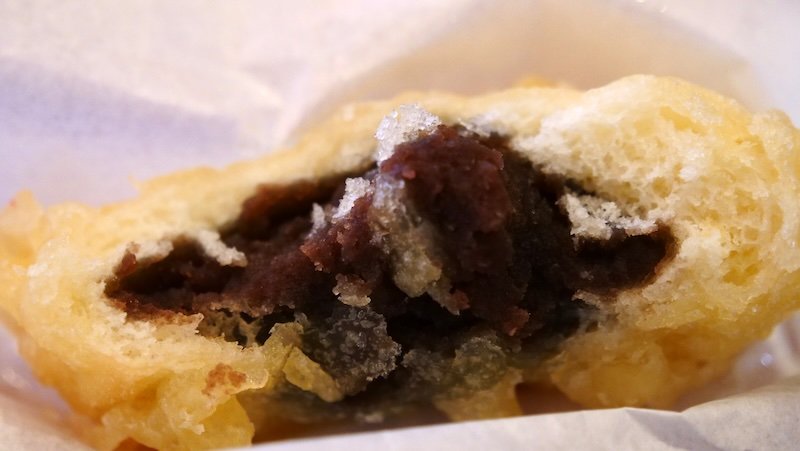 Close-up of a freshly fried manju pastry with a crispy golden batter and sweet anko red bean paste filling, a popular street food treat in Nikko, Japan