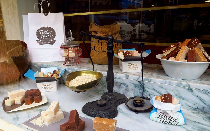 Window display at The Fudge House in Edinburgh, Scotland showcasing assorted handmade fudge pieces, scales, oats, and gift boxes