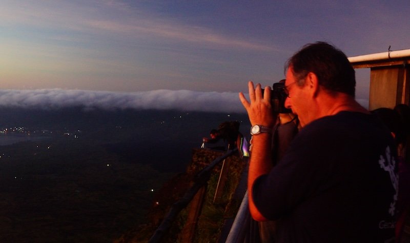 Nomadic Samuel’s father George photographing the breathtaking sunrise view from the summit of Mount Batur in Bali, Indonesia, with a sea of clouds and distant lights below