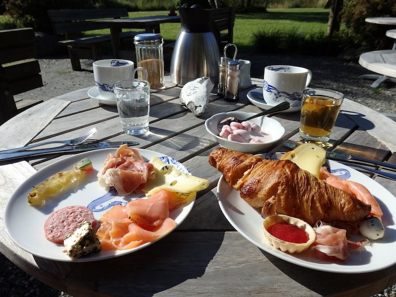 Delicious German-style breakfast spread on Rügen Island, Germany, featuring croissants, cold cuts, smoked salmon, assorted cheeses, salami, fresh fruit, yogurt with berries, and coffee served outdoors on a sunny patio table