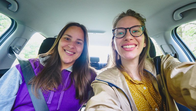 A cheerful selfie of two sisters sitting inside a car at the start of their weekend getaway to a cosy tiny cabin in Glen Huron, Ontario. Smiling at the camera, they capture the excitement of their road trip adventure surrounded by nature
