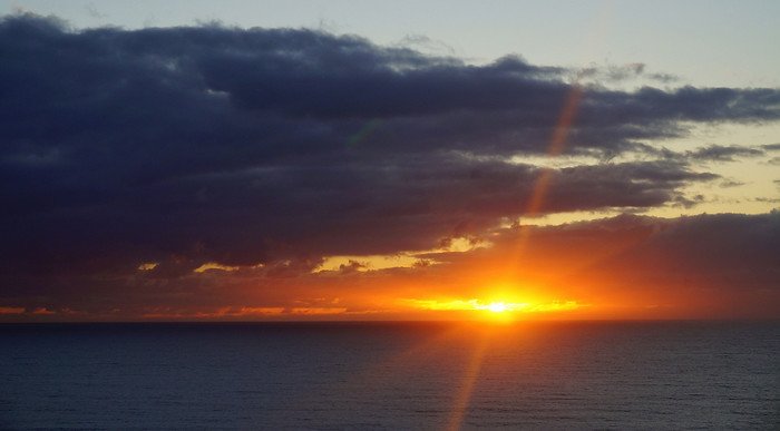 Golden sunset over the Gold Coast in Queensland, Australia, with the sun dipping below the horizon and casting warm orange light across the ocean under dramatic dark clouds
