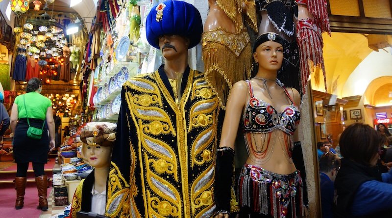 Colorful mannequins dressed in ornate Ottoman-style robes and glittering belly dance costumes on display at a vibrant stall in the Grand Bazaar of Istanbul, Turkey