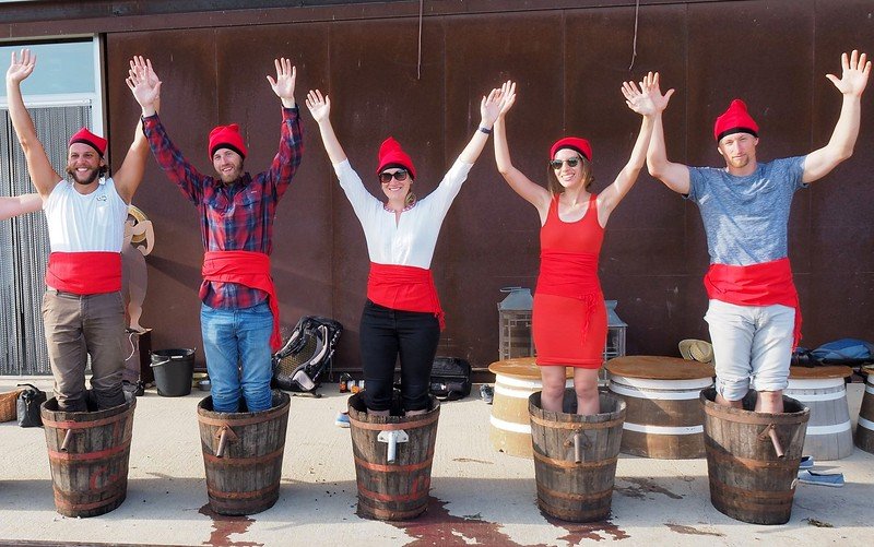 Group grape stomping at La Vinyeta winery in Costa Brava, Spain, with Audrey Bergner of That Backpacker, Brendan Van Son, and friends dressed in traditional Catalan outfits with red sashes and hats, celebrating winemaking culture during a vineyard tour