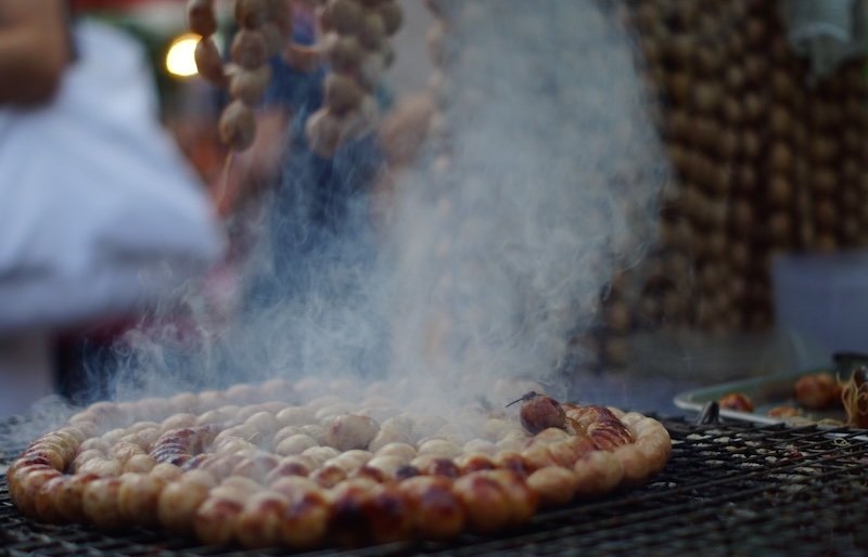 Grilled meat and sausages in Chiang Mai, Thailand as street food with steam rising like crazy from it being cooked at a high temperature 