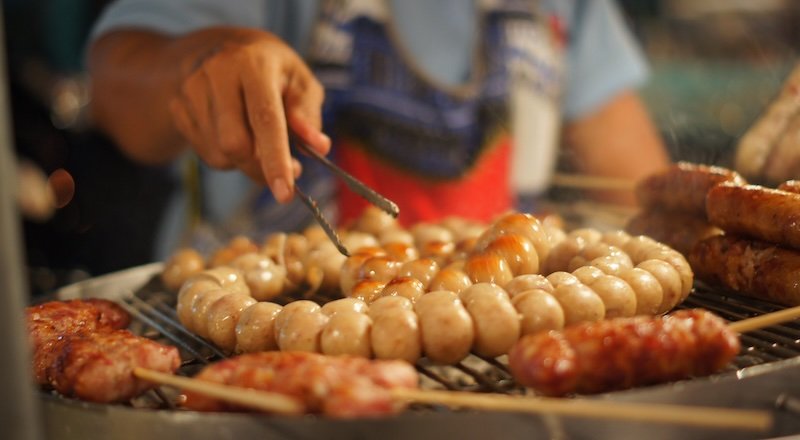 Grilled meat being sold at the Chiang Mai Saturday Night Market macro details of the vendor flipping the meat 