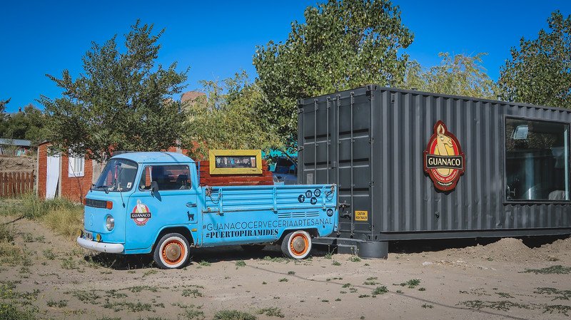 A bright blue vintage truck parked beside the Guanaco Brewery’s modern black shipping container in Puerto Pirámides, Patagonia. The playful design and craft beer branding highlight the town’s laid-back vibe and growing artisanal beer scene