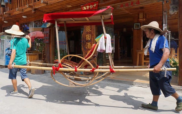 Hard working men of Ping'An, China carrying passengers on a sedan like wooden chair in the countryside