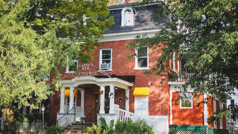 Charming red-brick heritage building with yellow awnings and Victorian architectural details surrounded by mature trees in Sutton, Quebec’s Eastern Townships