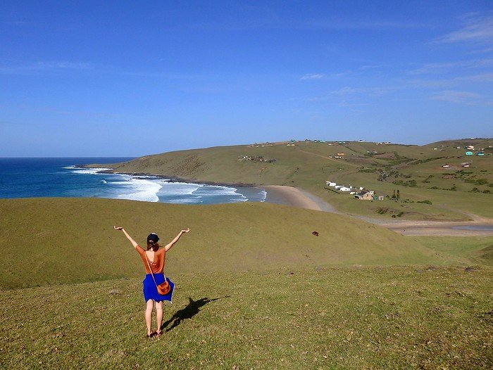Hiking in the Wild Coast, South Africa with incredible coastal views and a very happy That Backpacker Audrey Berger with arms stretched out 
