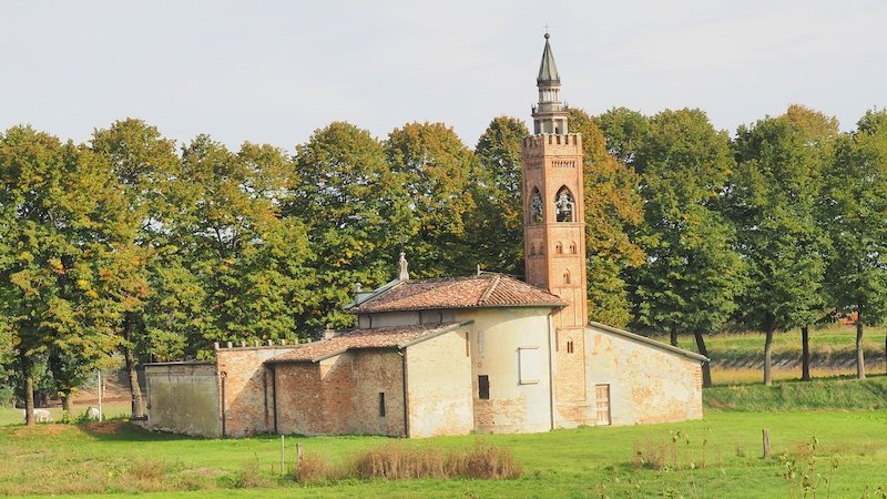 Historic countryside church with a tall bell tower surrounded by lush green fields and trees in Emilia-Romagna, Italy, showcasing the region’s cultural landmarks and rural charm that travelers discover while exploring food and heritage routes