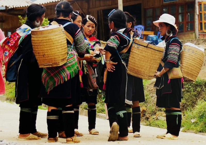 Group of local Hmong women in traditional embroidered clothing and carrying woven baskets gather on a village street in Sapa, Vietnam, showcasing the region’s vibrant hill tribe culture