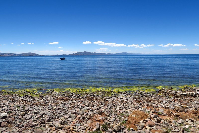 Homestay in Lake Titicaca, Amantani with rocky beach views and pristine clear water with mountains in the background and a boat off in the distance