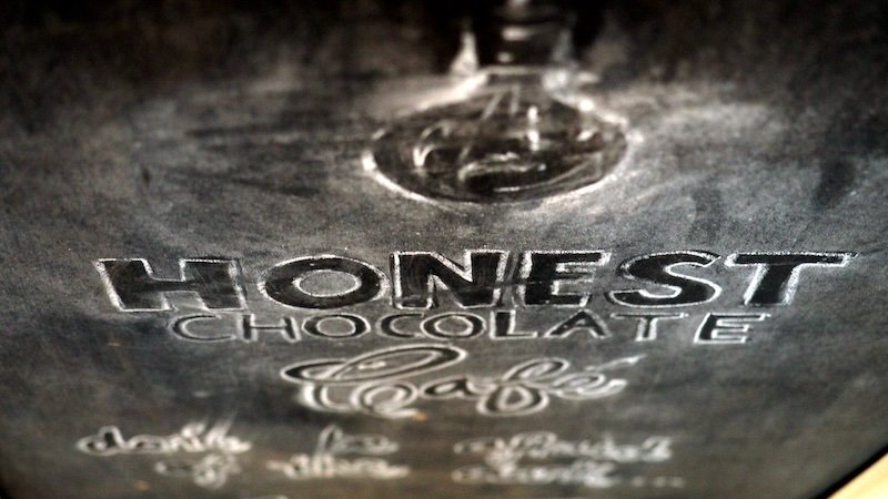 Close-up of a chalkboard sign with the Honest Chocolate Café logo and handwritten lettering, capturing the artisanal charm of this cozy spot in Cape Town, South Africa