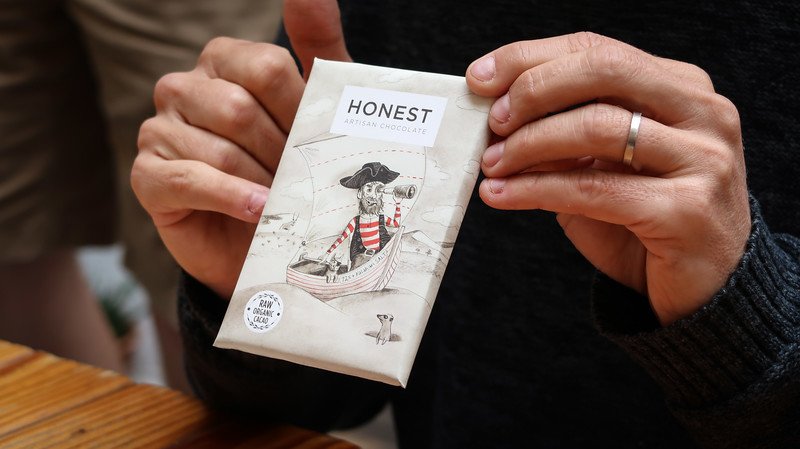 Close-up of hands holding a beautifully illustrated bar of raw, organic artisan chocolate from Honest Chocolate in Cape Town, known for its handcrafted bean-to-bar creations