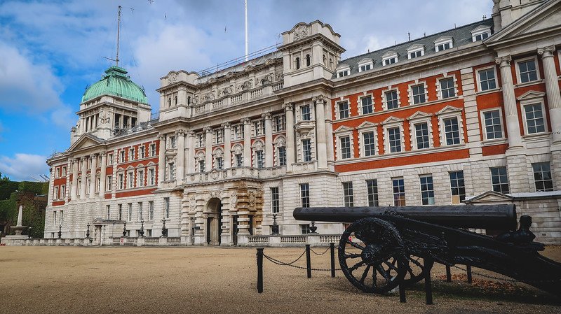 The grand historic building at Horse Guards Parade in London, featuring ornate red-and-white architecture with a green dome and a historic cannon in the foreground, symbolizing Britain’s military heritage and ceremonial traditions