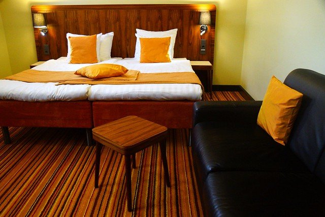 Cozy hotel room at Hotel Katajanokka in Helsinki, Finland, featuring a double bed with orange accents, striped carpet, and modern furnishings, blending the historic jailhouse’s unique character with contemporary comfort for an unforgettable stay
