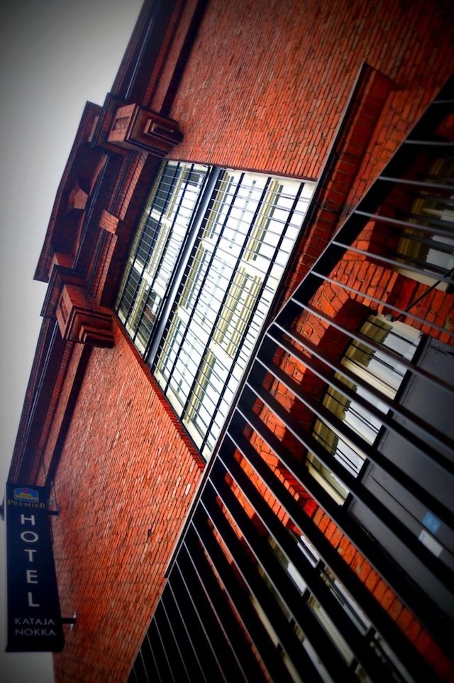 Dramatic angled view of Hotel Katajanokka in Helsinki, Finland, showing the historic red-brick prison architecture with barred windows and hotel signage, capturing the unique character of the former jail transformed into a modern boutique hotel