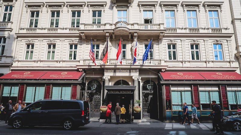 Elegant façade of Hotel Sacher in Vienna, Austria, adorned with flags and ornate architectural details, known as the birthplace of the iconic Sachertorte Elegant façade of Hotel Sacher in Vienna, Austria, adorned with flags and ornate architectural details, known as the birthplace of the iconic Sachertorte