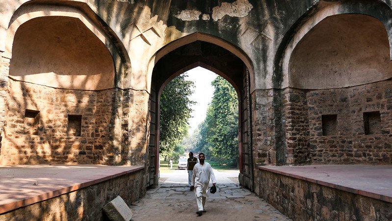 Visitors walking through an arched Mughal gateway at Humayun’s Tomb complex in Delhi, India, showcasing historic stone architecture