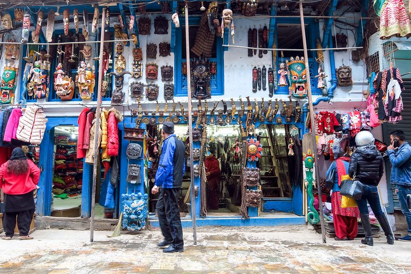 Colorful Indra Chowk Market in Kathmandu, Nepal with traditional wooden masks, handmade crafts, vibrant clothing, and curious shoppers exploring the stalls